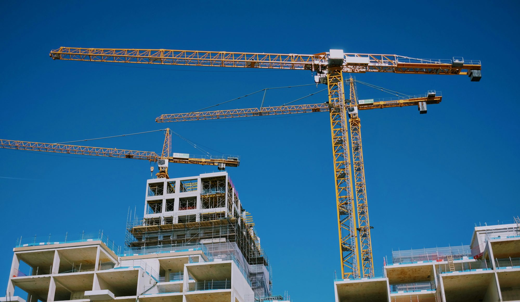 Gruas sobre estrutura de concreto em construção, com lajes e escoramento à vista