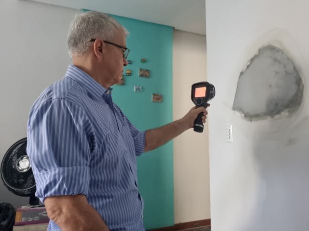 Engenheiro apontando câmera termográfica FLIR para parede com mancha de infiltração, verificando se o reparo foi eficaz.